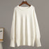 A cream oversized sweater displayed on wooden hanger against gray wall. Drop shoulder design with ribbed collar and cuffs visible