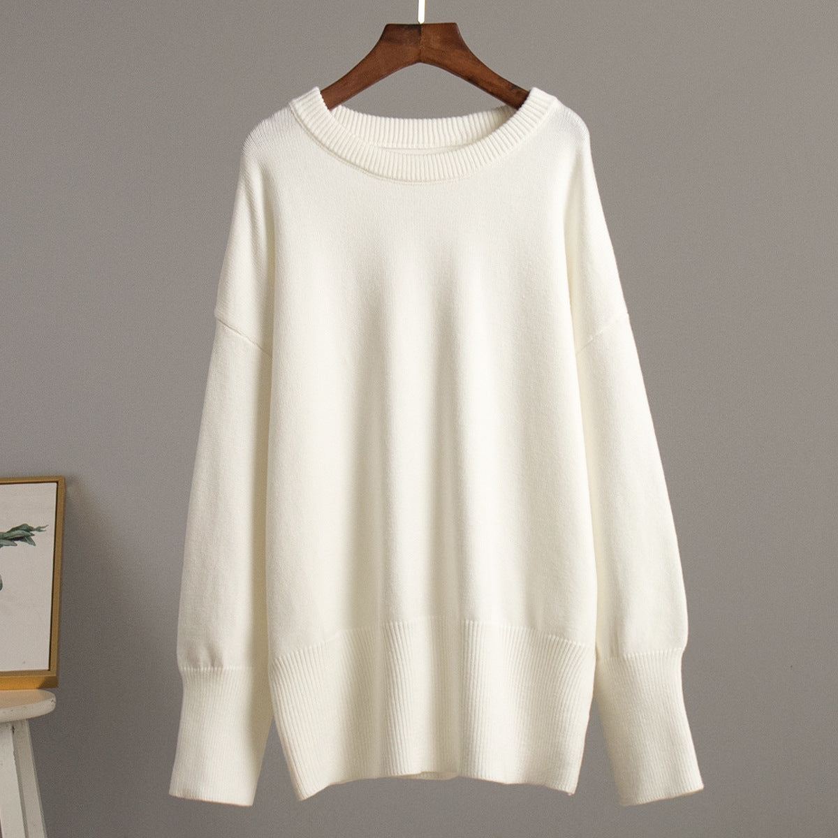 A cream oversized sweater displayed on wooden hanger against gray wall. Drop shoulder design with ribbed collar and cuffs visible