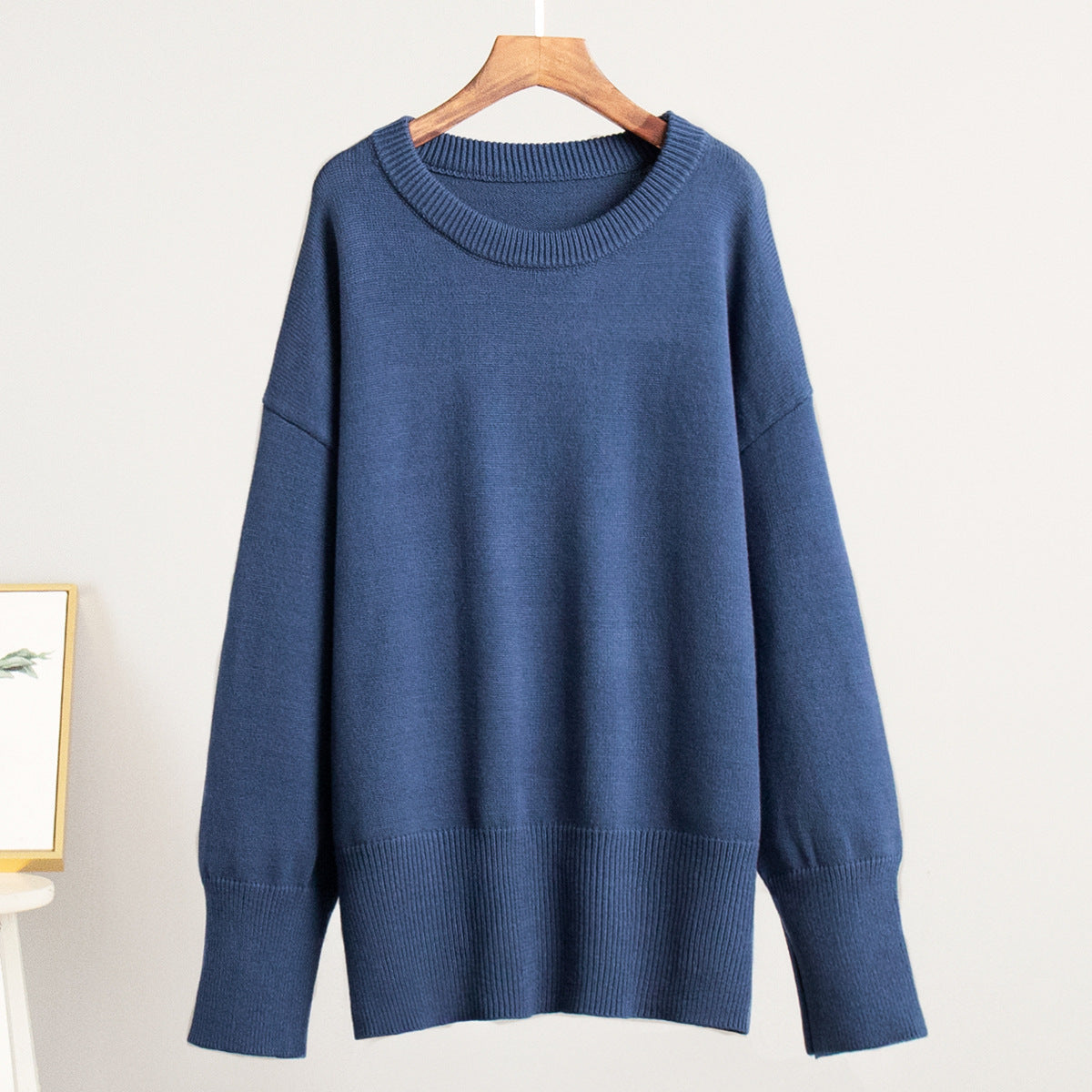 A navy blue oversized sweater displayed on wooden hanger against white wall. Relaxed fit with ribbed trim details and drop shoulders
