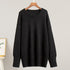 A black oversized sweater displayed on wooden hanger against light background. Classic crew neck with wide ribbed cuffs and hem