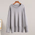 A light gray oversized sweater displayed on wooden hanger against neutral backdrop. Relaxed silhouette with ribbed detail at edges