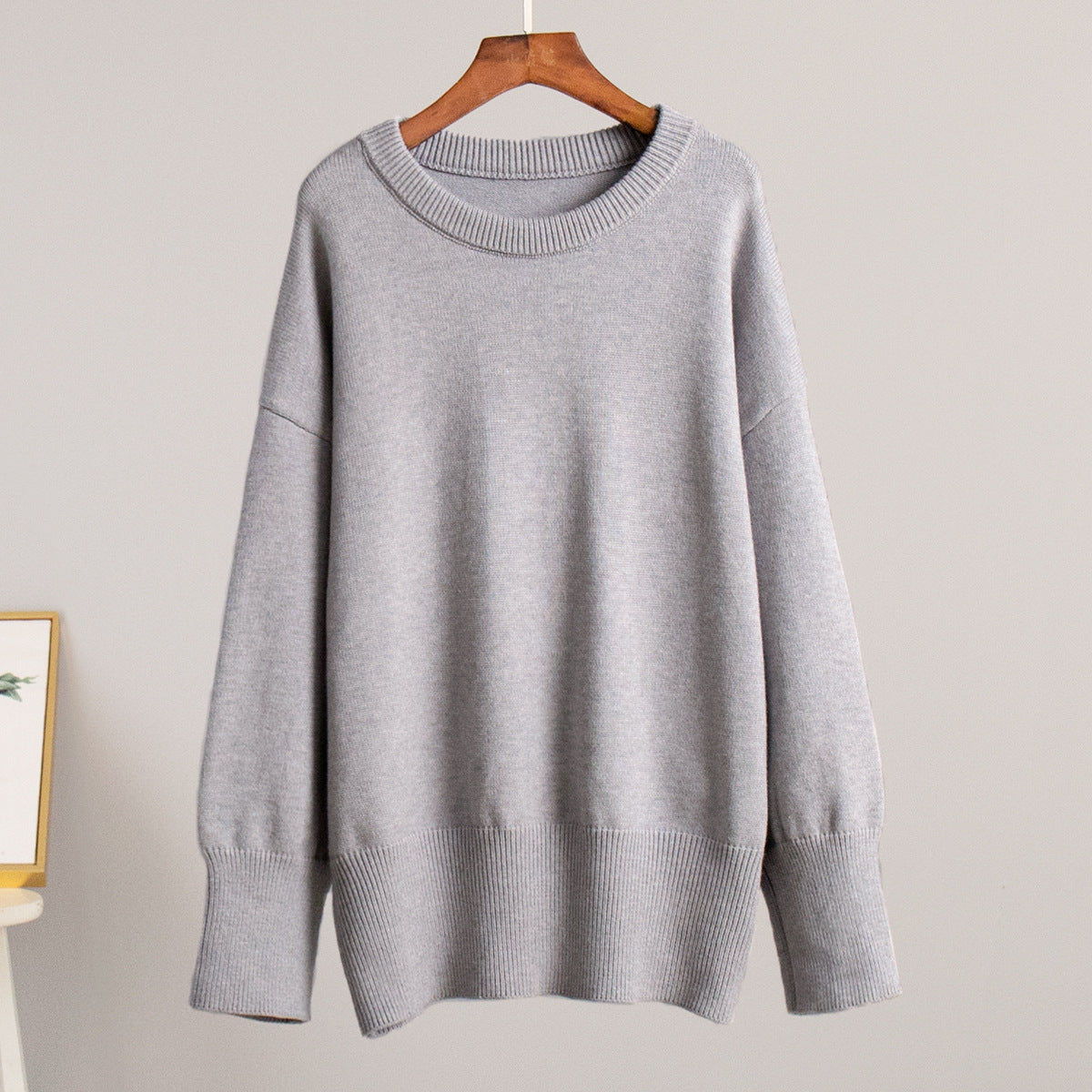 A light gray oversized sweater displayed on wooden hanger against neutral backdrop. Relaxed silhouette with ribbed detail at edges