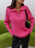 A woman is wearing a pink ribbed zip-collar sweater with black leather pants, posing in front of a green couch