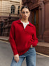 A woman is wearing a red ribbed zip-collar sweater with blue jeans, standing on a city street with historic architecture in the background