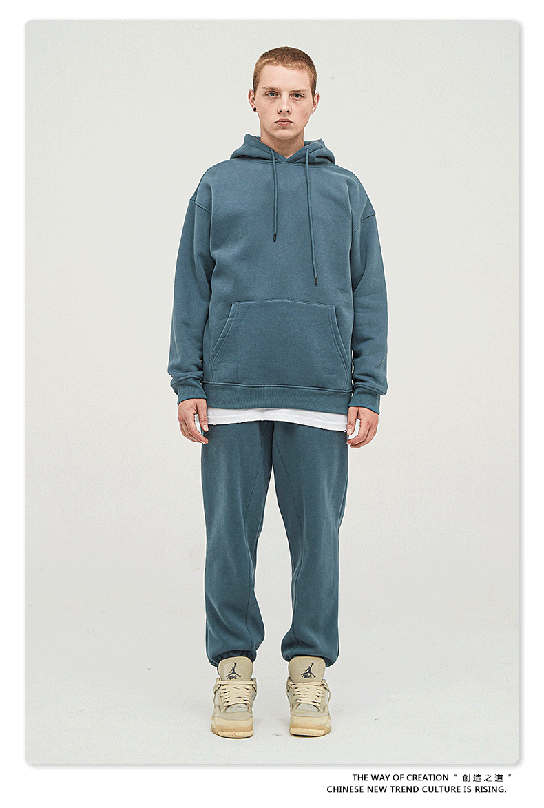 Male model with short hair wearing a slate blue sweatsuit with hoodie, white undershirt, and matching joggers