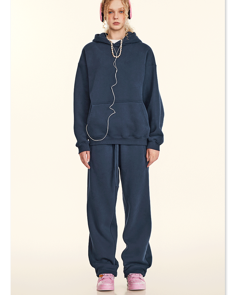 Model in navy hoodie and sweatpants set with pink headphones and matching sneakers on beige backdrop