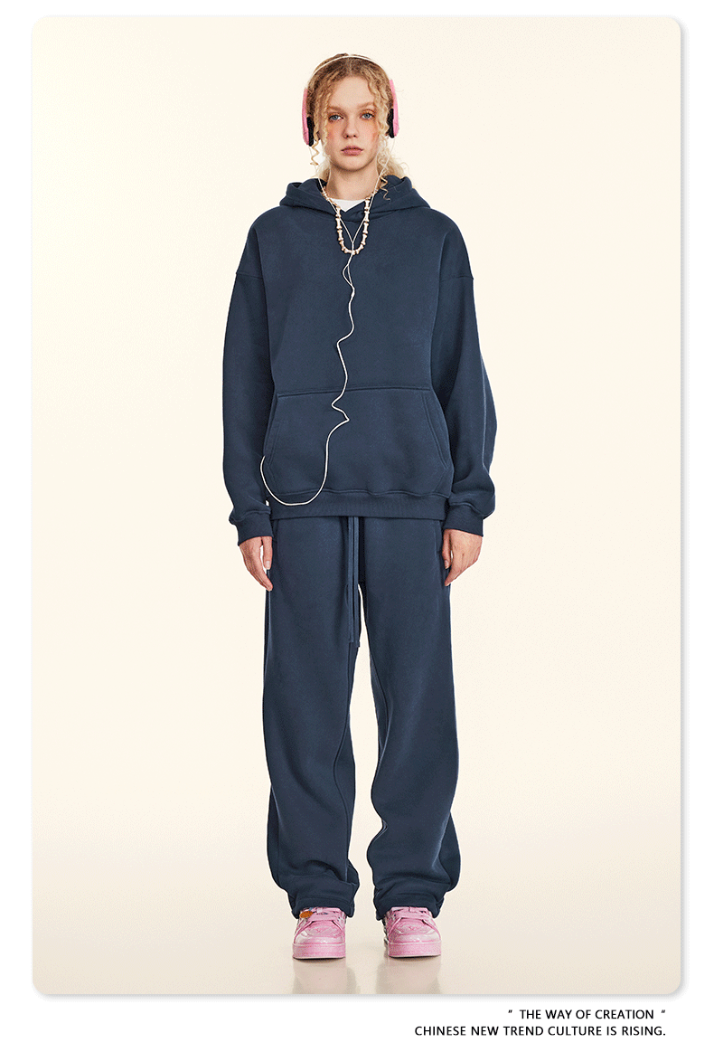 Model in navy hoodie and sweatpants set with pink headphones and matching sneakers on beige backdrop