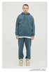 Male model wearing a teal blue sweatsuit with hood and front pocket, standing against white background with neutral expression