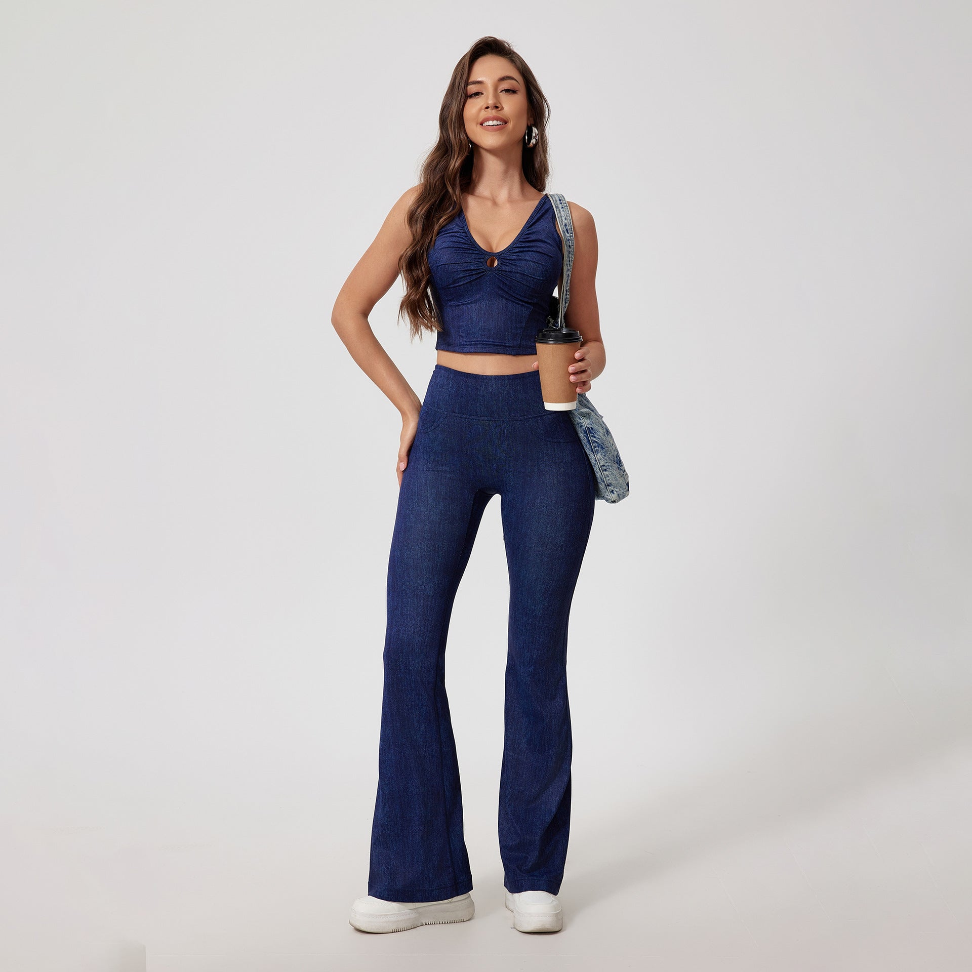 Dark denim coordinated set featuring cropped tank top with ruched v-neck and flared pants, styled with white sneakers