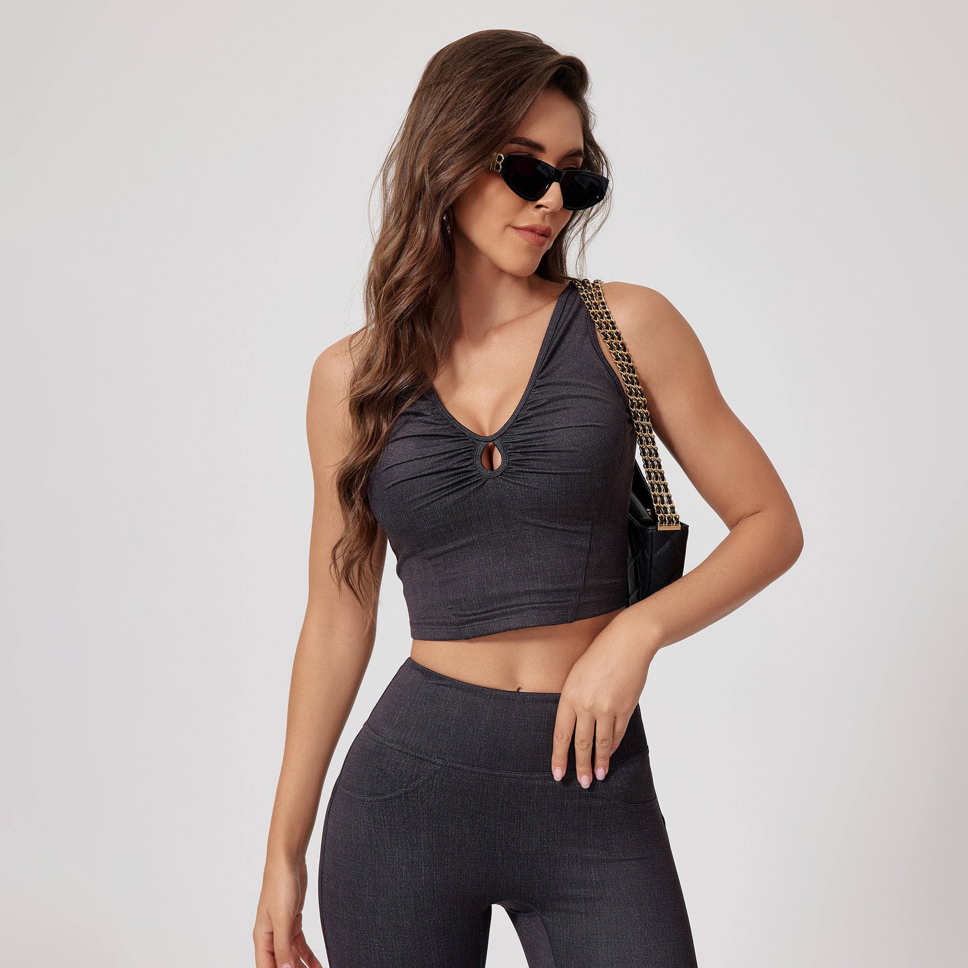 Dark denim athleisure set featuring ruched crop top and high-waisted leggings, accessorized with chain-strap bag