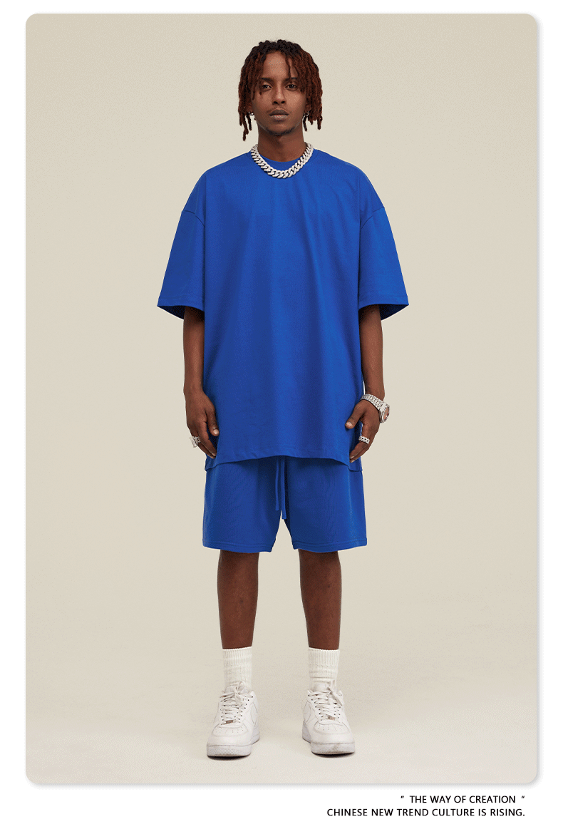 Man wearing royal blue oversized T-shirt and shorts set with white Air Force 1 sneakers and silver chain