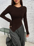 Dark brown asymmetrical long-sleeve top with angular design, styled with gray cargo pants against white brick wall