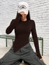 Model in white New York cap, brown asymmetrical top, and gray cargo pants, hand partially covering face