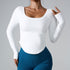 A model wearing a white long-sleeve fitted top with scoop neckline, paired with blue high-waisted athletic leggings, posing against gray backdrop