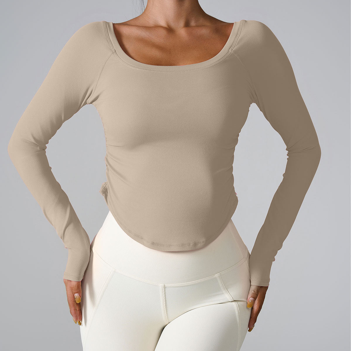 A model wearing a beige long-sleeve fitted top with scoop neck, paired with cream-colored high-waisted leggings, against neutral gray background