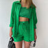 A model is wearing a bright green three-piece loungewear set, including a button-up shirt, a crop top, and drawstring shorts, while holding a black handbag