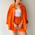 A model is wearing an orange three-piece loungewear set with a white ribbed crop top, posing with hands clasped in front against a white background