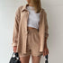 A model is wearing a beige three-piece loungewear set with a white crop top, holding black sunglasses and a black handbag