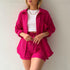 A model is wearing a fuchsia pink three-piece loungewear set with a white crop top, accessorized with gold jewelry and multiple rings