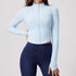 Woman wearing a light blue ribbed zip-up cropped jacket with long sleeves and a high collar, paired with dark blue leggings