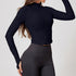 Side view of a woman in a black ribbed zip-up cropped jacket with long sleeves and thumb holes, paired with dark leggings