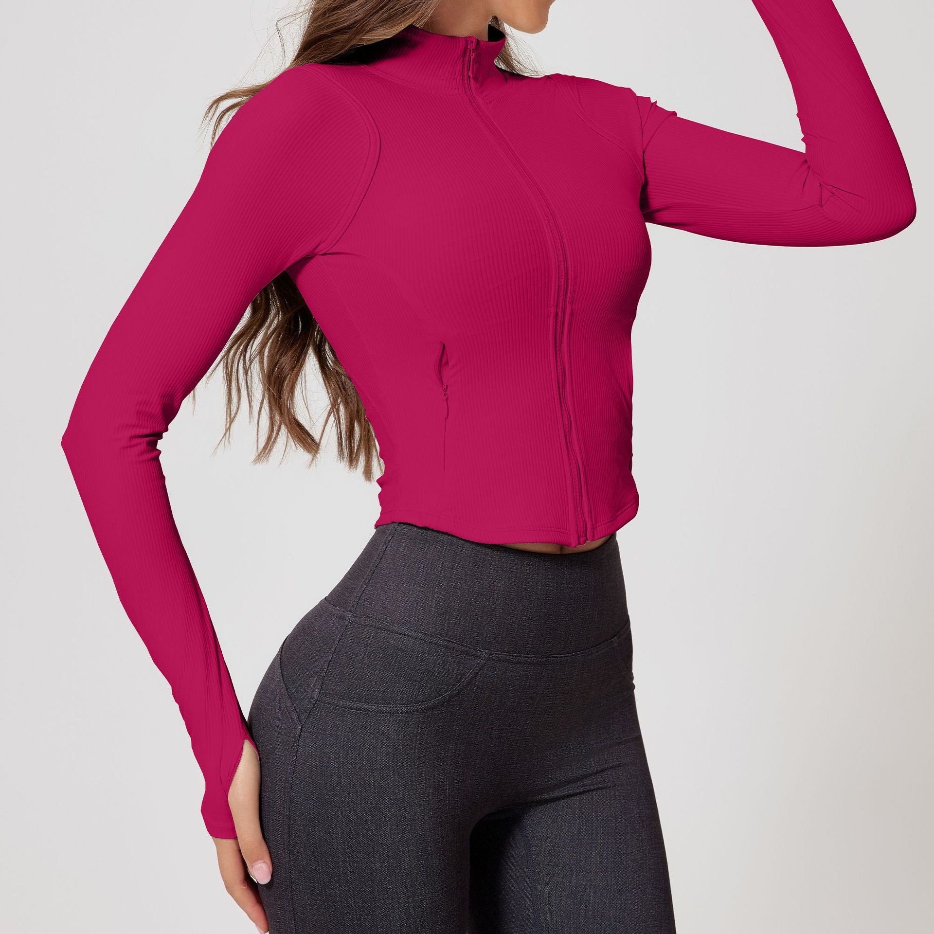 Woman wearing a vibrant pink ribbed zip-up cropped jacket with long sleeves and a sculpted fit