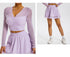 A model is wearing a lavender mesh-sleeve crop top with V-neckline and matching mini skirt, full-length view showing white sneakers against a gray background