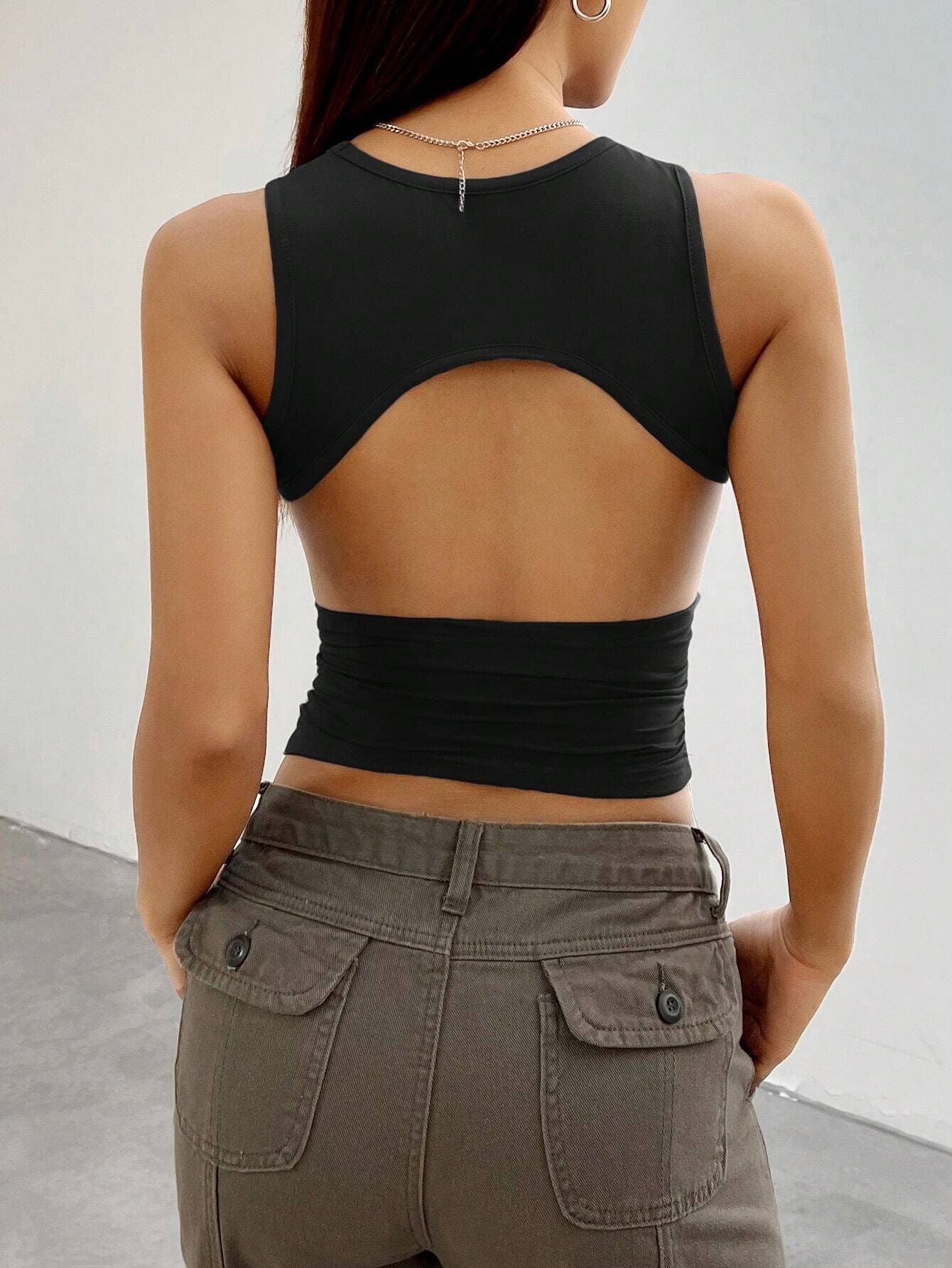 Back view of black crop top revealing distinctive cut-out design, paired with olive cargo pants