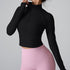 A woman wearing a black ribbed half-zip crop top with long sleeves and mock neck paired with pink high-waisted leggings against a neutral backdrop