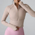 A woman wearing a nude ribbed half-zip crop top with mock neck and long sleeves paired with pink leggings, touching collar against gray background
