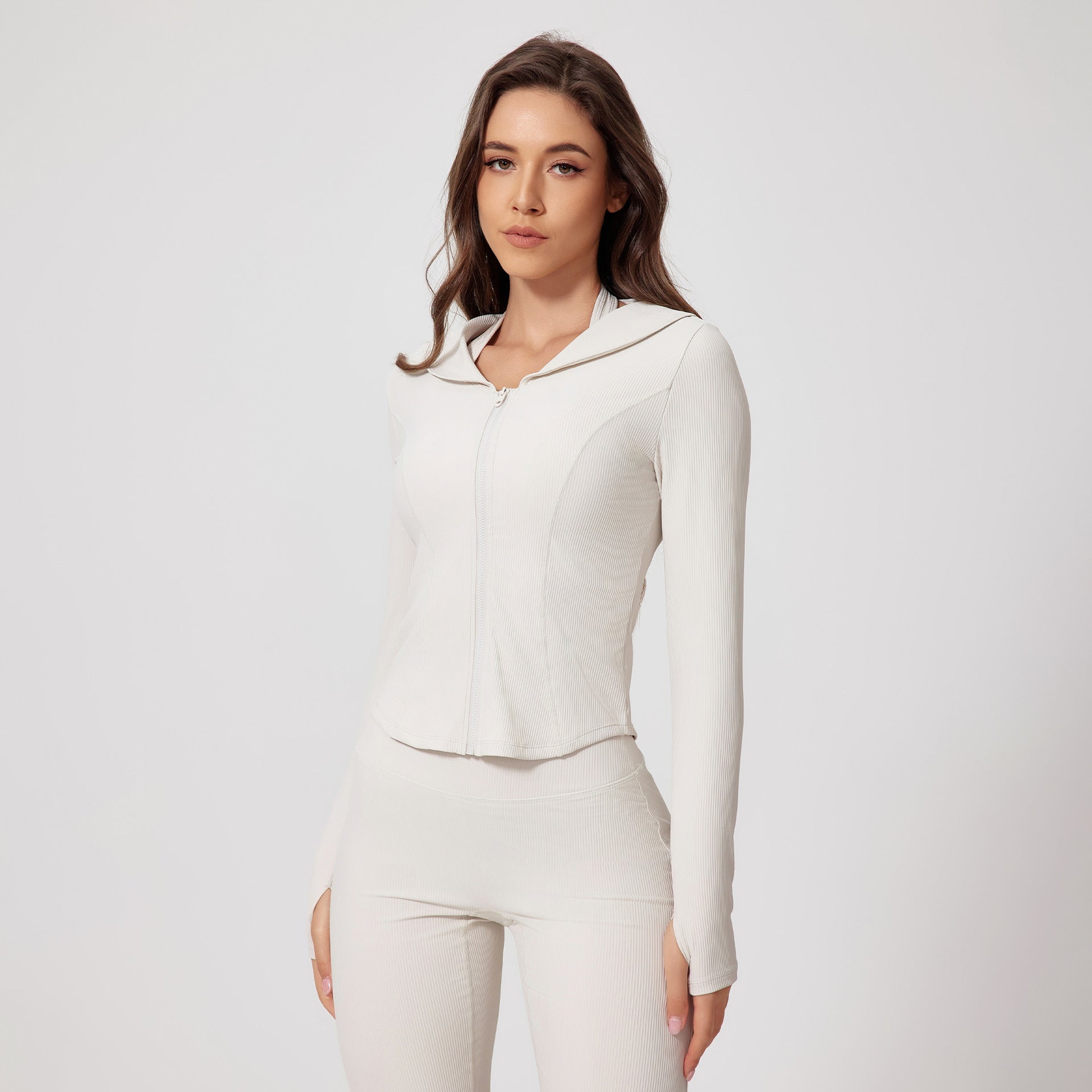 Woman modeling a white ribbed activewear set with zip-up jacket and matching leggings with thumb holes