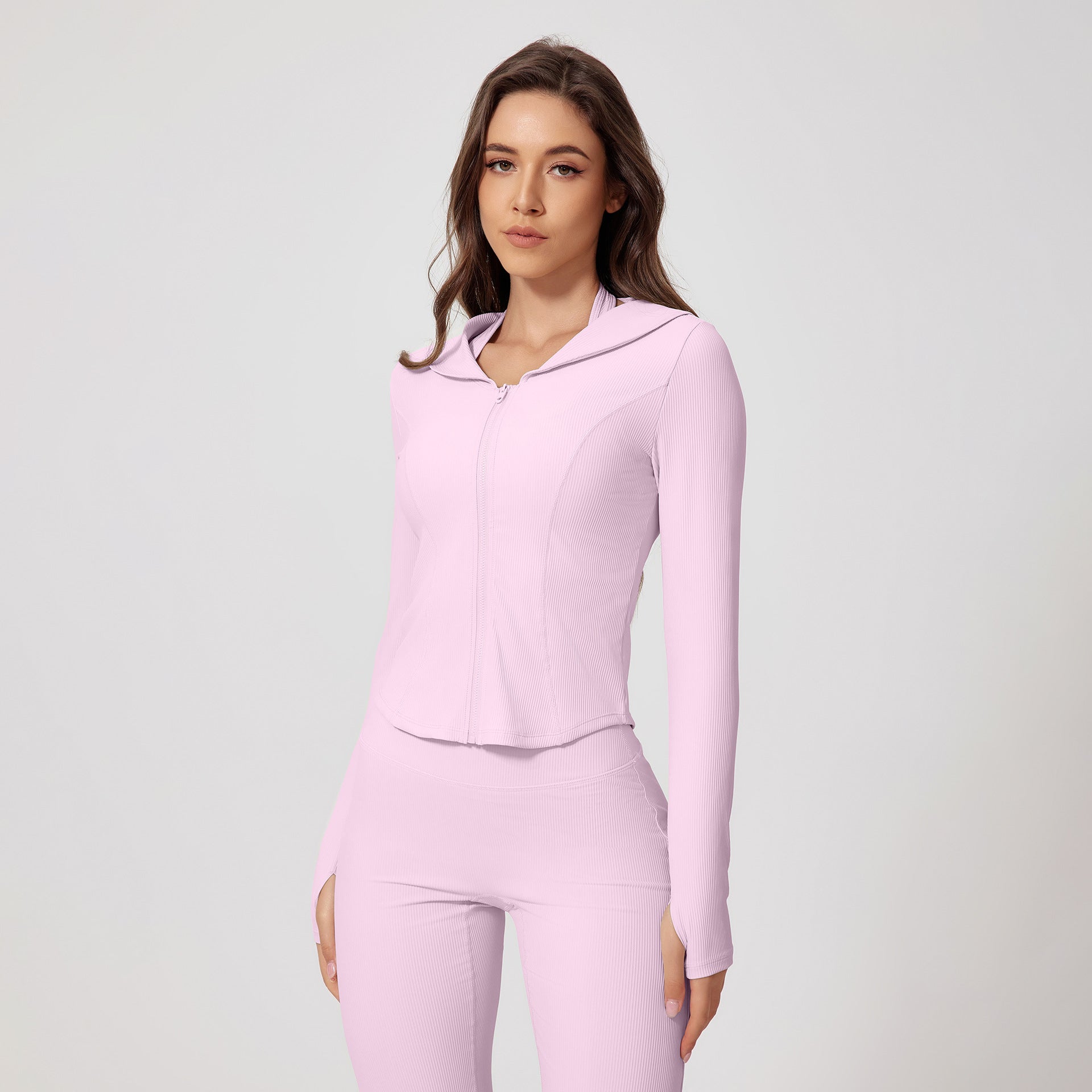 Model wearing a light pink ribbed workout set with hooded zip jacket and high-waisted leggings with thumb holes