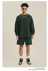 Man in forest green sweatshirt and shorts set with sunglasses, necklace and white sneakers