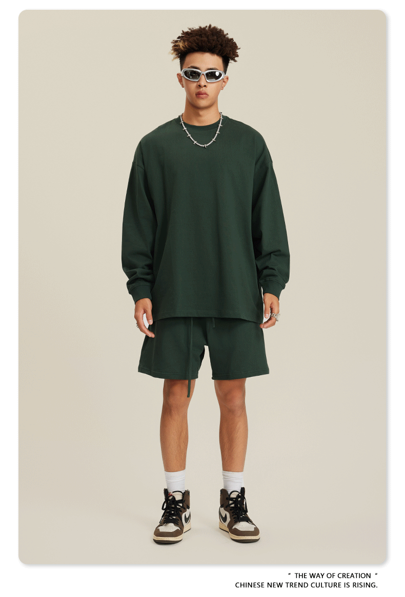 Man in forest green sweatshirt and shorts set with sunglasses, necklace and white sneakers