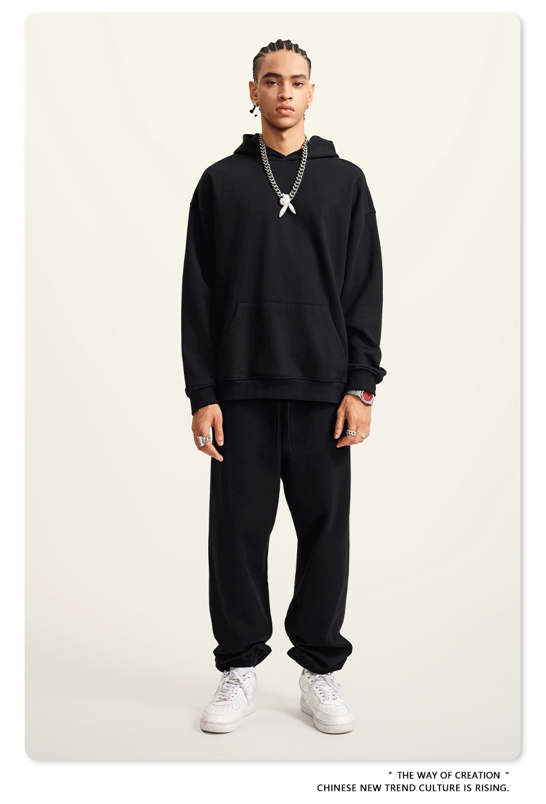 Man with braids wearing black hoodie and pants with silver chain pendant and white sneakers