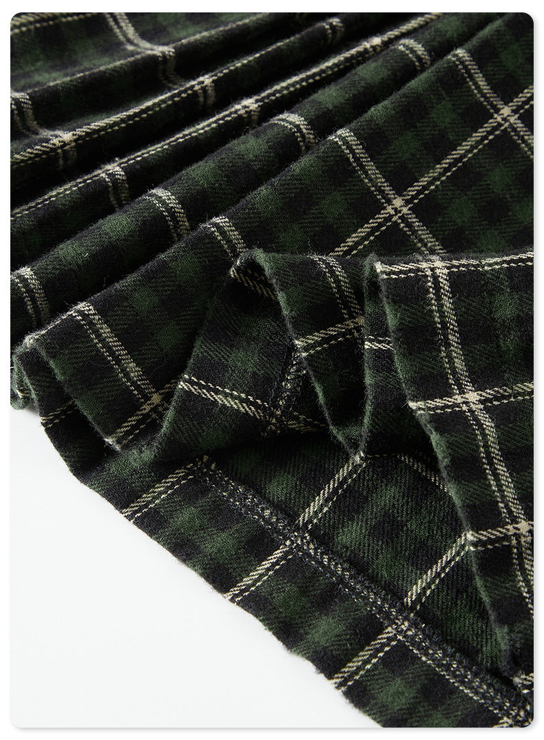 Close-up of pleated green plaid fabric showing texture and stitching against dark background