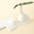A seamless, lightly padded white bra with a deep V-neck, displayed with a eucalyptus branch on a neutral background.