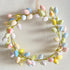 A decorative Easter egg wreath hanging on a white wall, featuring multicolored speckled eggs and a natural vine base.