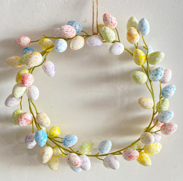 A decorative Easter egg wreath hanging on a white wall, featuring multicolored speckled eggs and a natural vine base.