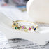 A gold rainbow bubble ring featuring colorful gemstones resting on white ceramic surface with book page visible
