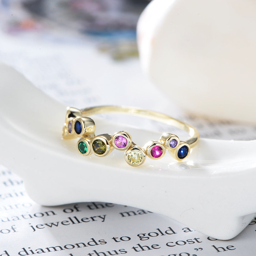 A gold rainbow bubble ring featuring colorful gemstones resting on white ceramic surface with book page visible