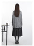 Back view of grey cable-knit sweater showing full length and distressed hem detail, worn with dark charcoal midi skirt and heeled pumps