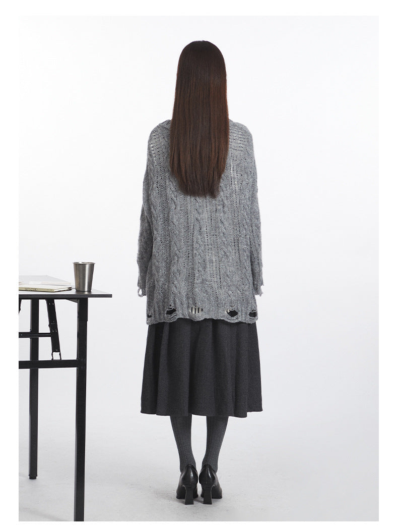 Back view of grey cable-knit sweater showing full length and distressed hem detail, worn with dark charcoal midi skirt and heeled pumps