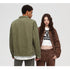 A woman wearing brown denim set and white graphic tee poses beside man shown from behind in olive denim jacket