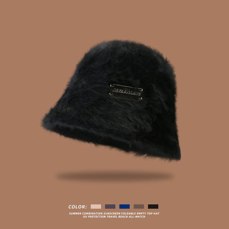 Black fluffy bucket hat with a black logo patch, displayed against a brown background