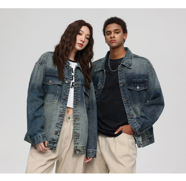A woman and man are standing close together against a gray backdrop. Both wearing faded blue denim trucker jackets over cropped tops with matching beige pants