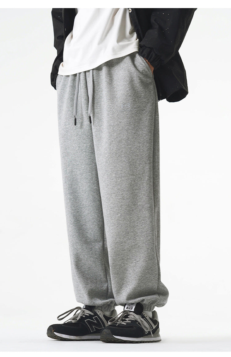 A model is wearing gray sweatpants with a relaxed fit, elastic cuffs, and a small embroidered logo