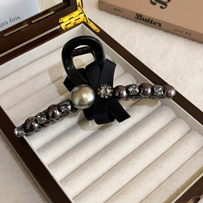 A black hair claw clip featuring a satin bow, dark pearls, and crystal embellishments for a chic, sophisticated look.