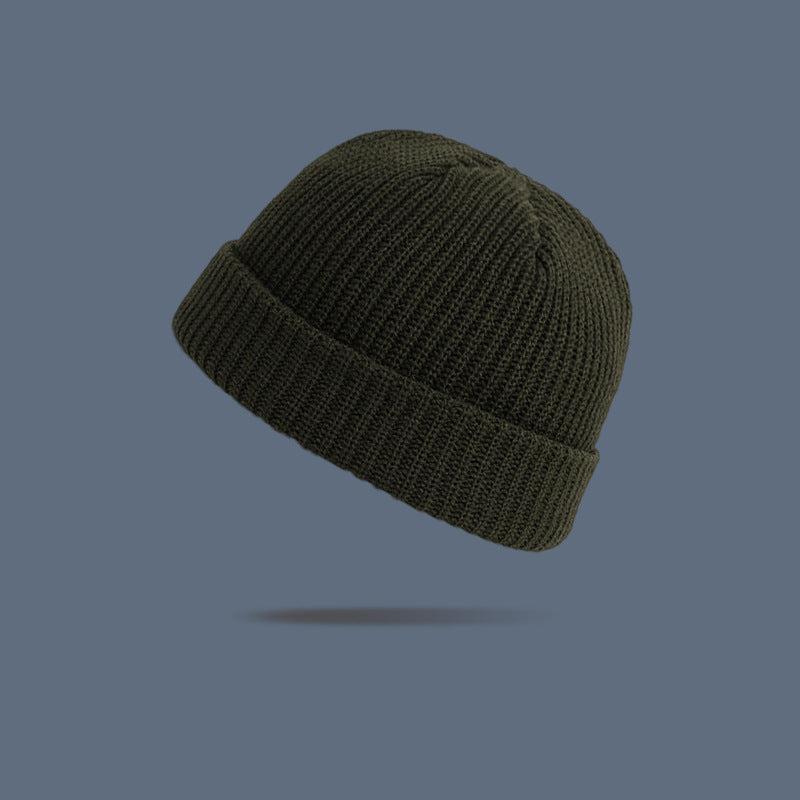 A army green ribbed knit beanie with folded cuff floating against slate gray background, displaying classic winter hat design
