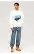 A model wearing white 'REPRESENT' shark graphic hoodie, relaxed-fit blue jeans and tan work boots, posing against white backdrop